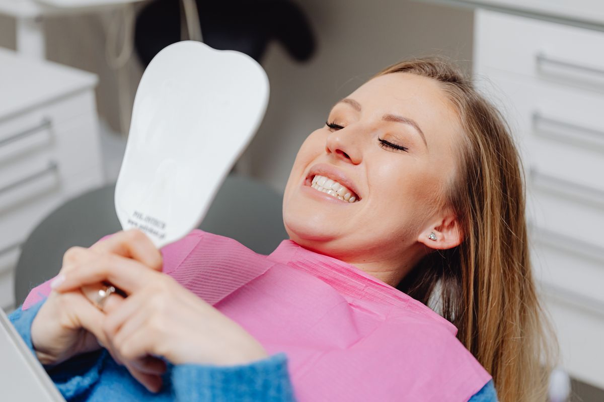 Patient smiling at her teeth in a hand mirror after a dental check-up